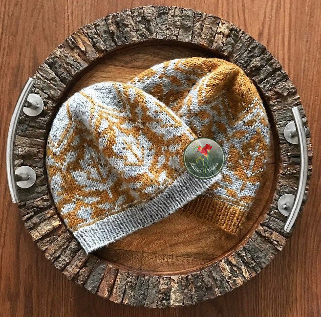 Knitted stranded colorwork beanie with a maple leaf pattern on a wooden tray