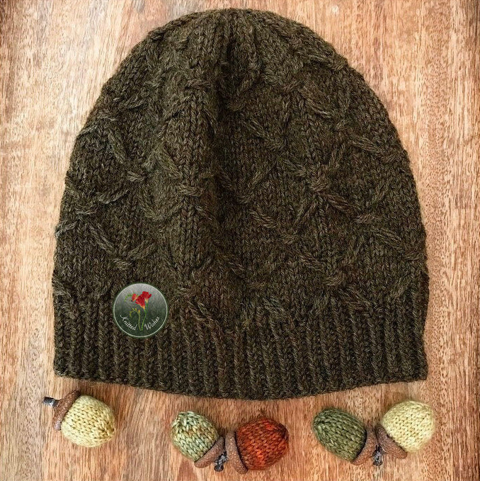 Knitted textured beanie on a wooden surface, surrounded by small knitted acorns.