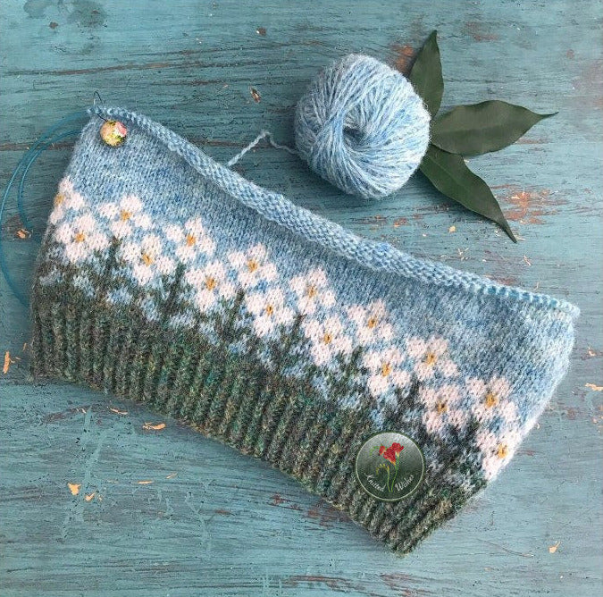 Knitted colorwork hat with floral pattern on a wooden surface with yarn ball and leaves.