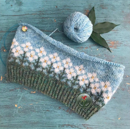 Knitted colorwork hat with floral pattern on a wooden surface with yarn ball and leaves.