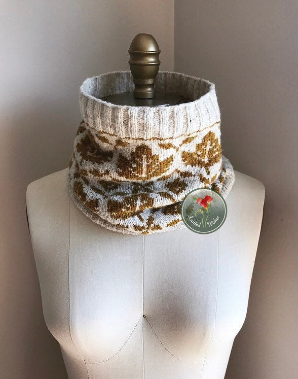 Knitted colorwork cowl with a maple leaf pattern on a mannequin with a plain background