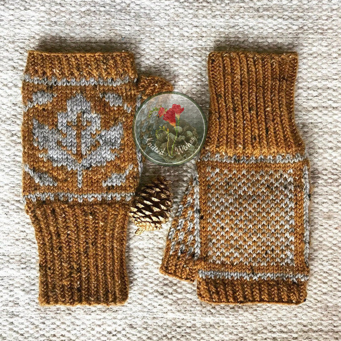 Pair of knitted fingerless mitts with a maple leaf pattern on a textured surface.