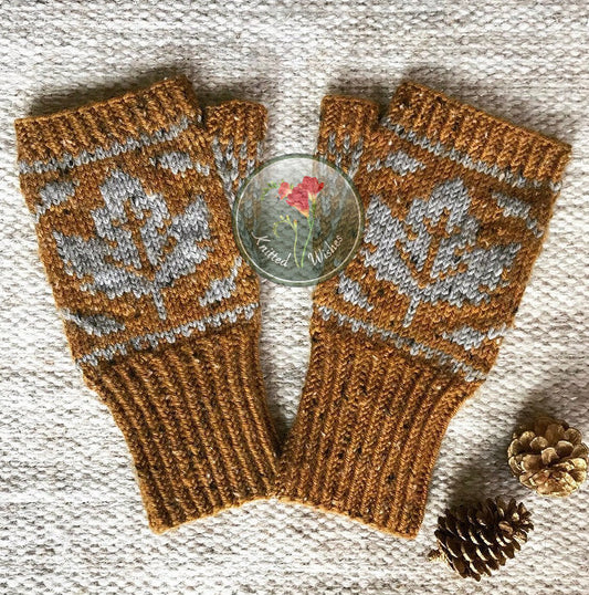 Pair of knitted mittens with a maple leaf design on a textured surface.