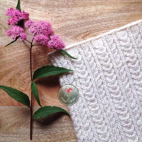 Knitted textured cowl and pink flowers on a wooden surface