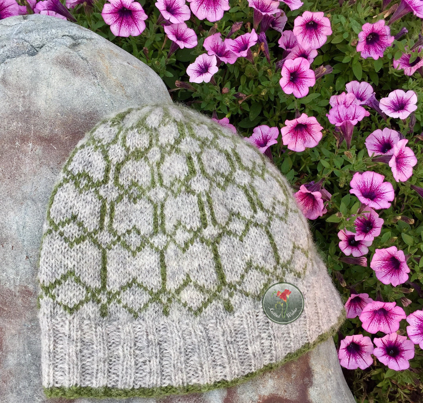 Knitted colorwork beanie with a patterned design on a stone surface with pink flowers in the background