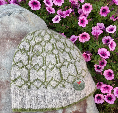 Knitted colorwork beanie with a patterned design on a stone surface with pink flowers in the background