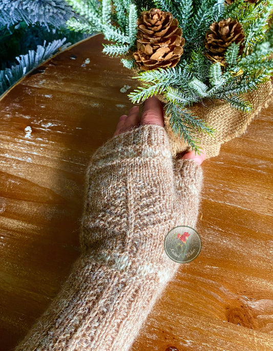 Hand wearing a textured knitted mitt holding a small Christmas tree on a wooden surface.