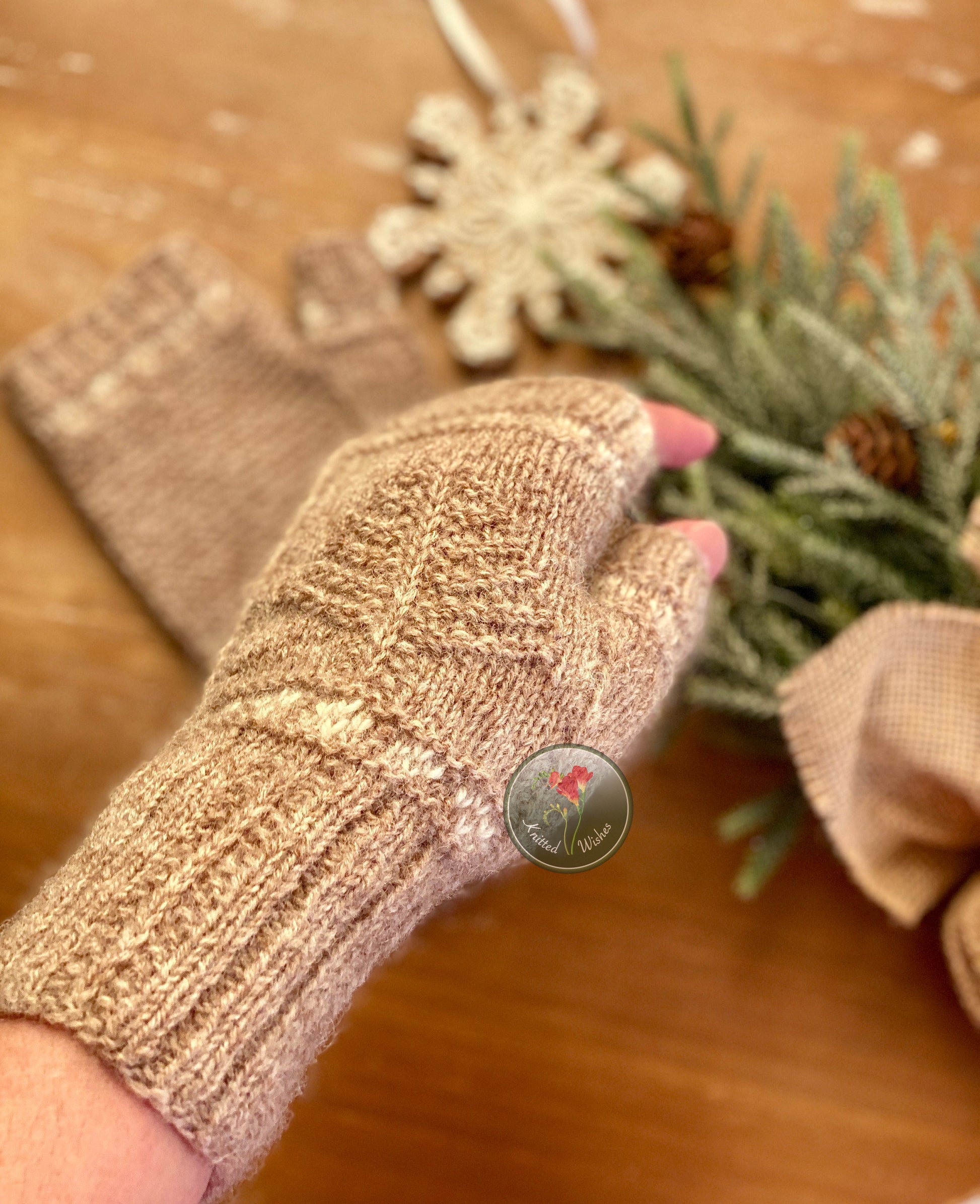 Hand wearing a fingerless kntted mitt with a blurred background of greenery and a decorative item.
