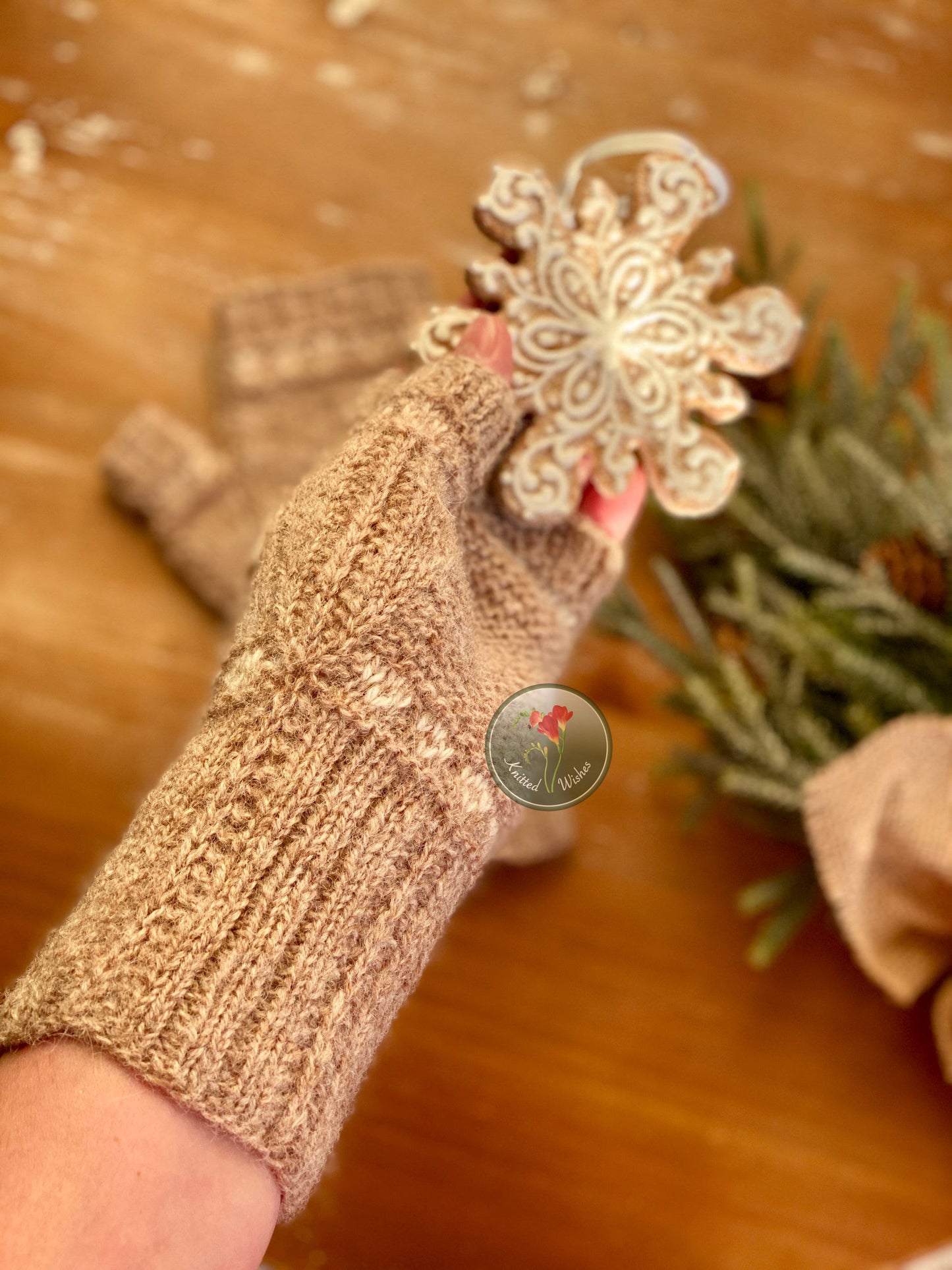 Hand wearing a textured brown fingerless mitt holding a decorative snowflake ornament on a wooden surface.