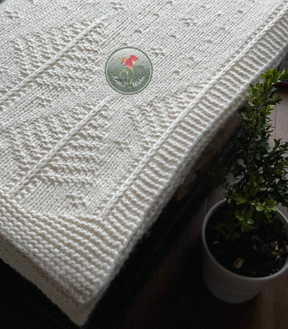 White textured knitted tree blanket on a wooden surface next to a potted plant.