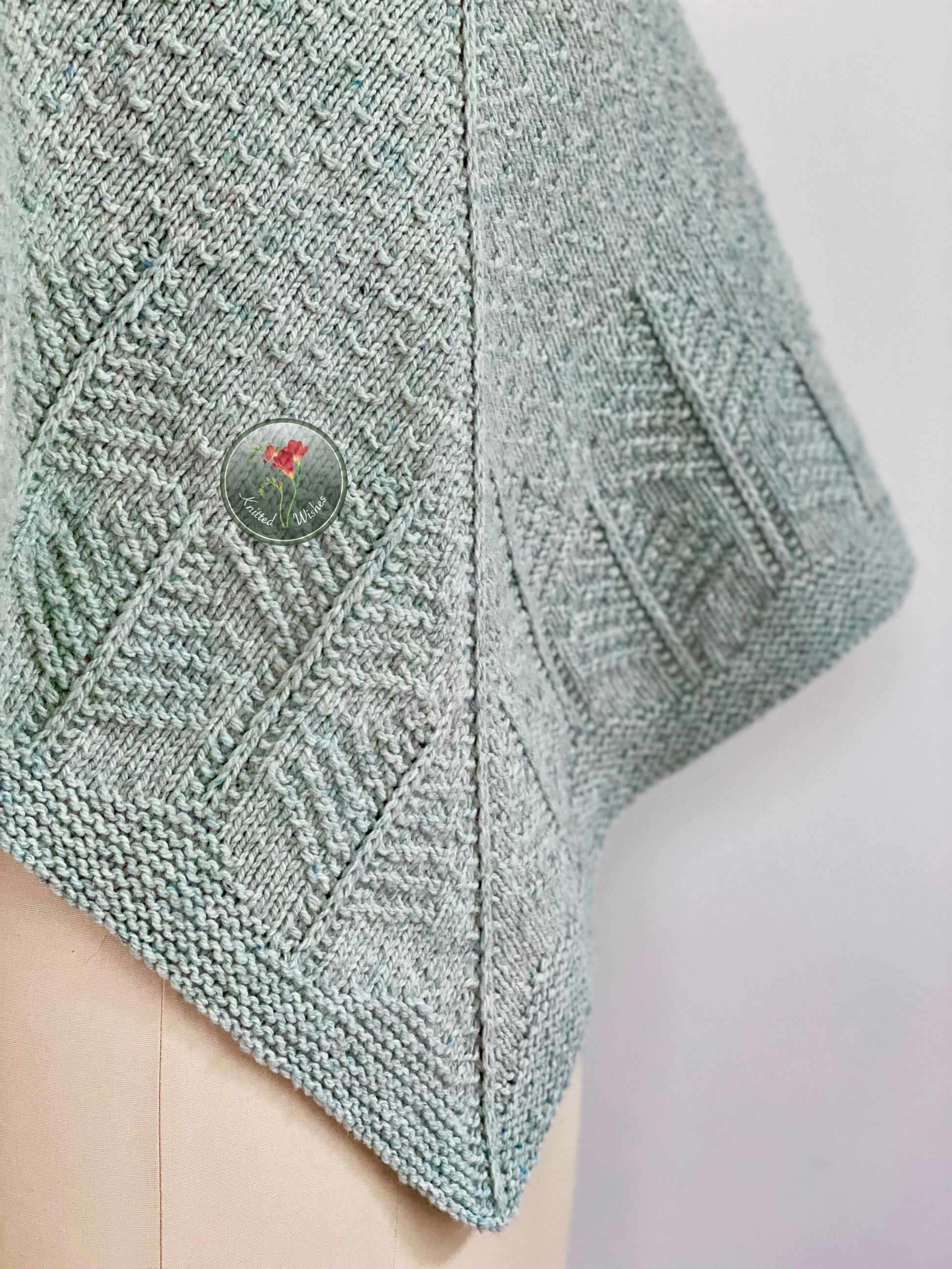 Light blue knitted shawl with a textured tree pattern on a white background