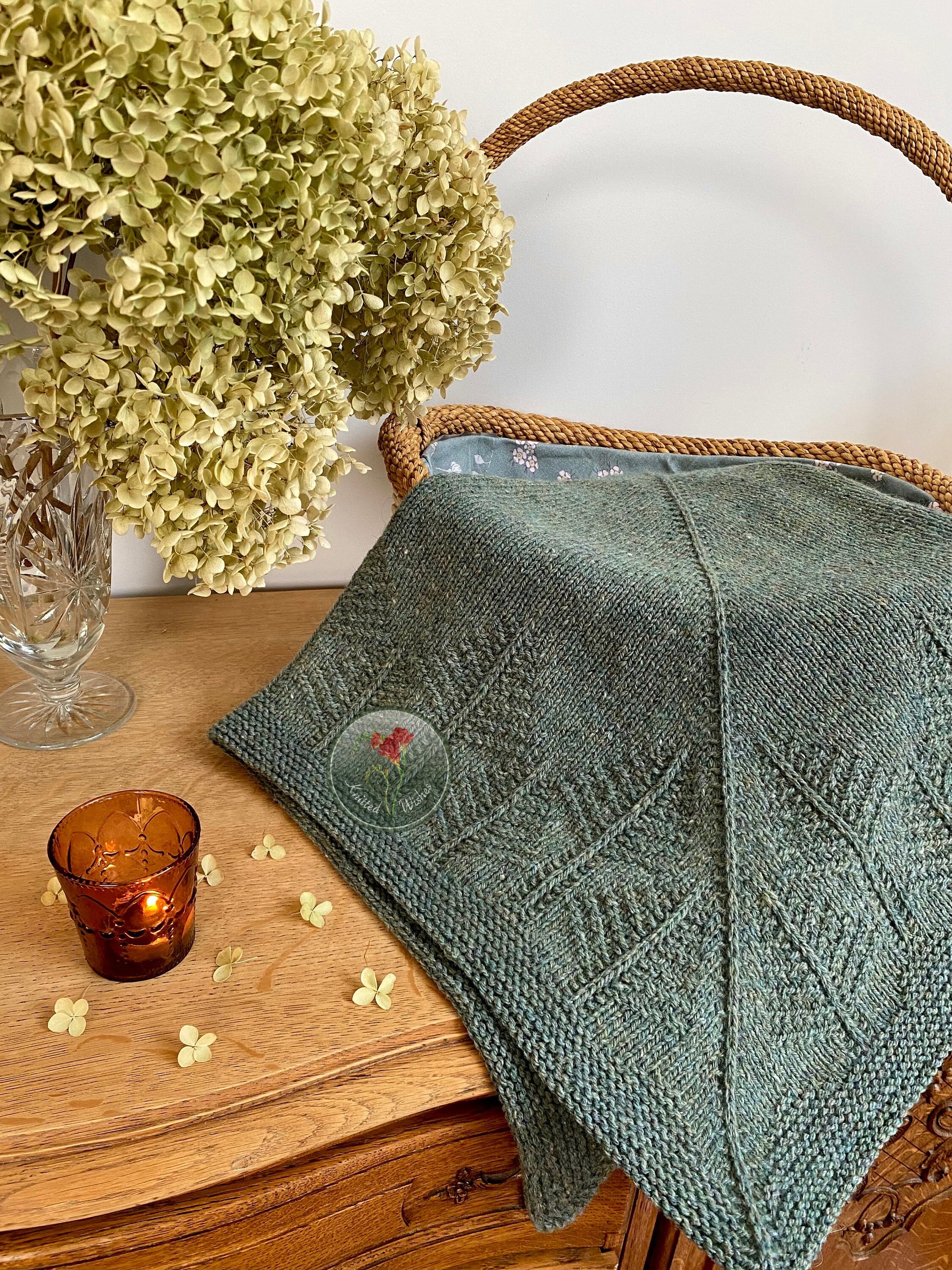 Green knitted textured shawl with a tree pattern on a wooden surface with flowers and a candle.