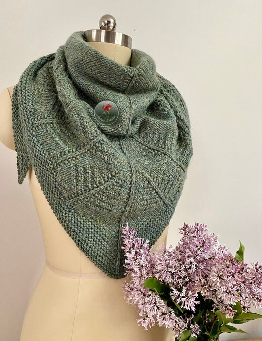 Green textured knitted shawl on a mannequin with a bouquet of flowers against a plain background