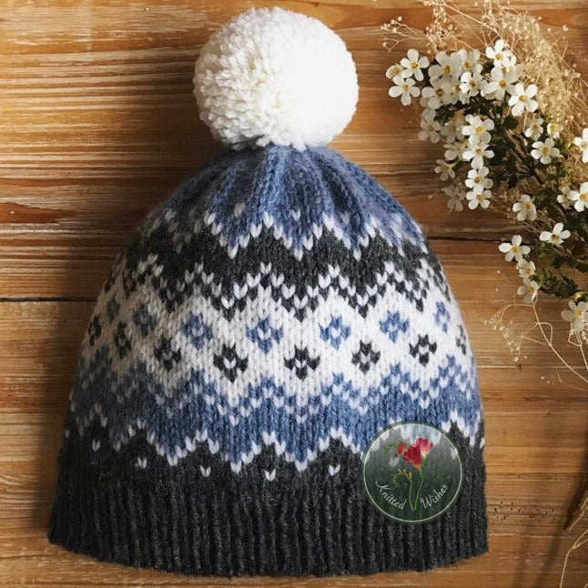 Knitted colorwork  hat with a white pom-pom on a wooden surface with flowers