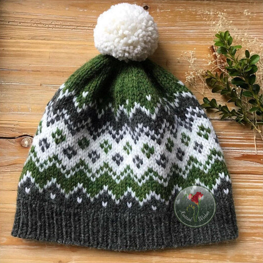 Knitted colorwork hat with a white pom-pom on a wooden surface