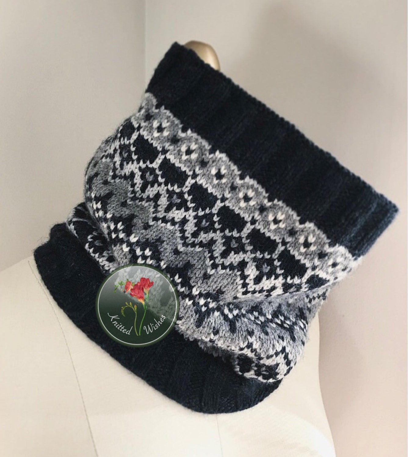 Black and gray patterned knitted cowl on a mannequin with a brand label.