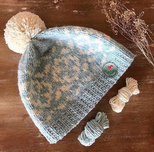 Knitted colorwork beanie with floral pattern and pom-pom on a wooden surface