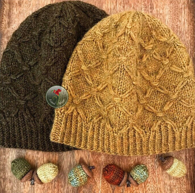 Two textured knitted hats, one yellow and one green, on a wooden surface with small knitted acorns.