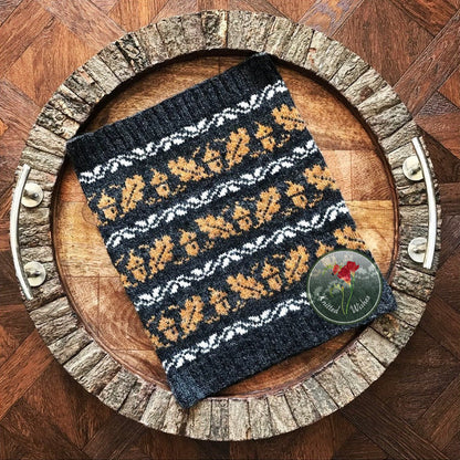 Knitted cowl with an acorn and oak leaf pattern on a wooden tray